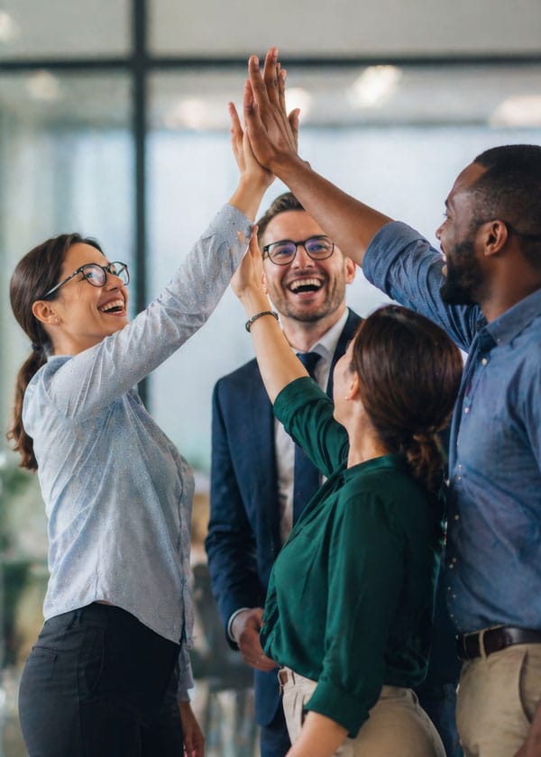A diverse group of coworkers high-fiving in an office, celebrating a success.